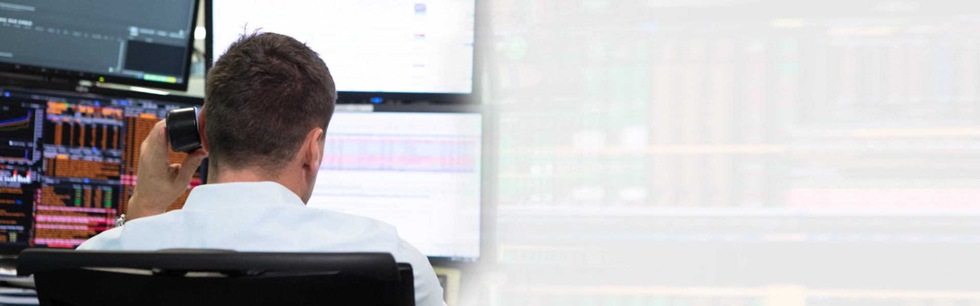 Das Bild zeigt eine Person, wahrscheinlich einen Börsenhändler oder Finanzanalysten, die vor mehreren Computerbildschirmen sitzt. Auf den Bildschirmen sind komplexe Diagramme und Daten visualisiert, die wahrscheinlich mit Finanzmärken und einem Handelsumfeld zu tun haben. Der Fokus des Bildes liegt auf der back der Person, die konzentriert arbeitet, und den Instrumenten des Finanzhandels, die detaillierte Analyse und Echtzeitüberwachung erfordern.